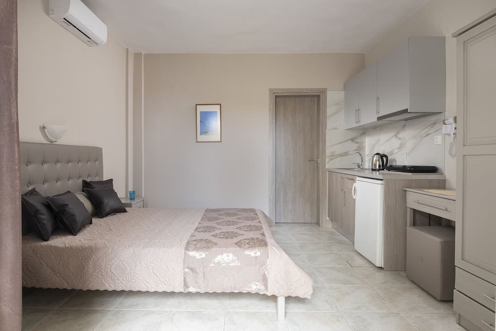 A cozy studio apartment features a neatly made bed, a compact kitchenette with marble backsplash, and neutral tones, ideal for travelers seeking comfort and convenience in a self-contained space.