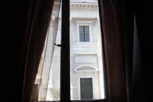 A serene view of a classical building facade framed by draped curtains through a window, ideal for travelers seeking historic architecture photography opportunities.