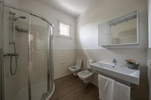 A cozy, modern bathroom with a glass-enclosed shower, wooden flooring, and white fixtures creates a serene atmosphere, ideal for travelers seeking comfort in a compact space.