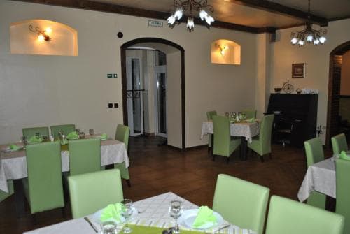 A cozy indoor restaurant with warm lighting, green chairs, wooden floors, and a piano in the corner creates an inviting atmosphere perfect for intimate dining experiences.