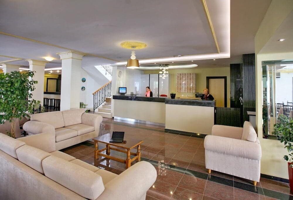 A cozy hotel lobby features plush beige sofas, a wooden coffee table, and a reception desk with friendly staff, creating a welcoming atmosphere ideal for travelers seeking comfort and hospitality.