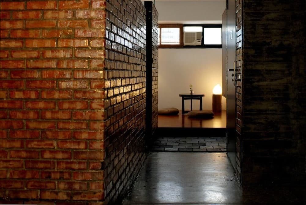 A serene indoor meditation space features exposed brick walls, a minimalist wooden table with a candle, and cushioned seating, ideal for travelers seeking tranquility and mindfulness retreats.