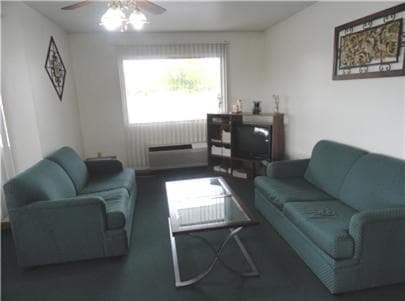 A cozy living room with teal sofas, a glass coffee table, and framed artwork exudes a relaxed atmosphere, ideal for travelers seeking a comfortable rental space.