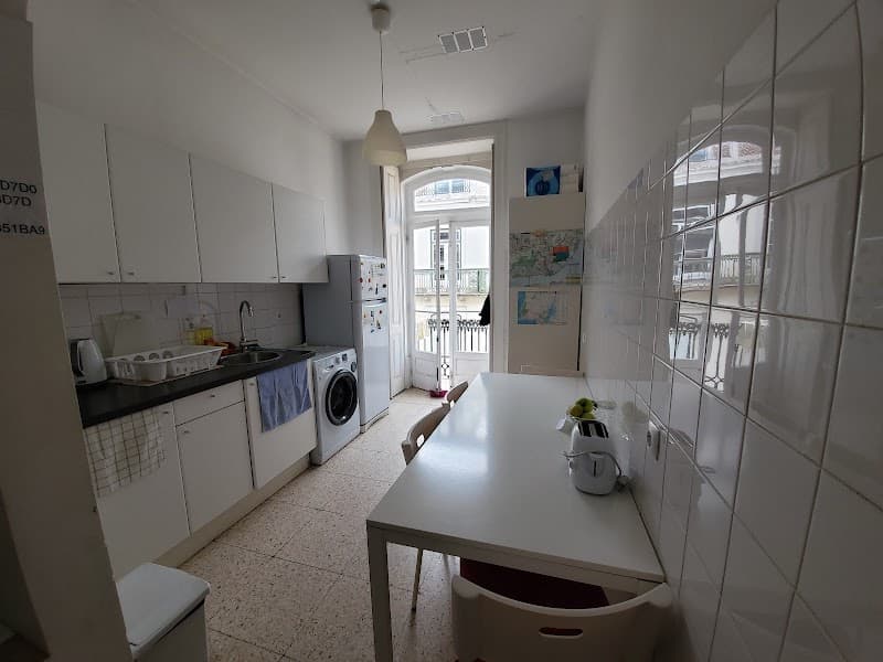 A cozy kitchen area in Lisbon's RiverView Hostel features white cabinetry, a dining table with chairs, and a balcony view, ideal for travelers seeking a comfortable and functional space for their stay.