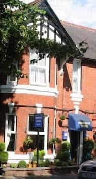 A charming red-brick Victorian-style building adorned with greenery and hanging baskets exudes a welcoming atmosphere, ideal for travelers seeking a cozy bed and breakfast experience in a quaint suburban setting.