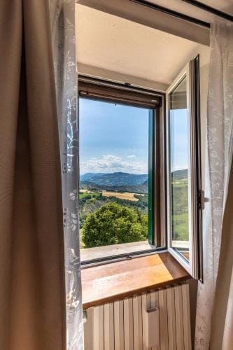 A serene view of rolling hills and distant mountains framed by an open window with sheer curtains, ideal for travelers seeking peaceful countryside retreats.