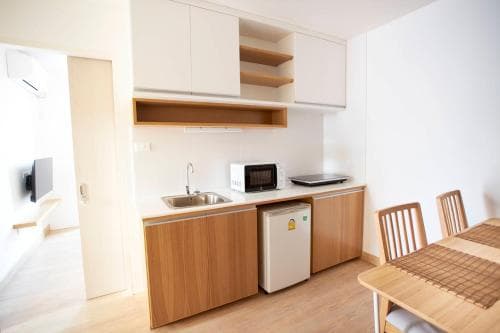 A cozy apartment kitchenette with wooden cabinets, a small fridge, and a dining table creates a warm and inviting atmosphere, ideal for travelers seeking a comfortable self-catering stay.