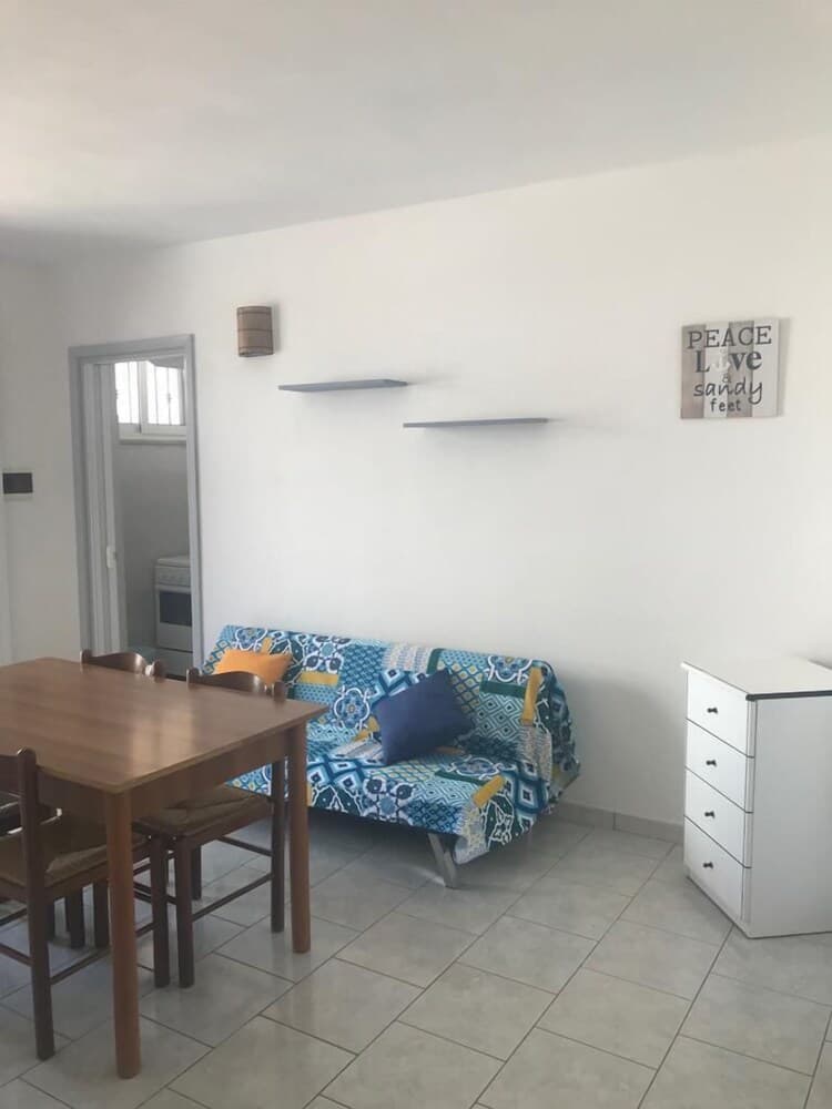 A cozy apartment living space features a patterned sofa, wooden dining set, and minimalist decor, ideal for travelers seeking a comfortable and affordable stay.