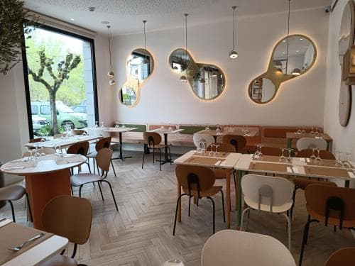 A cozy, modern café with stylish oval mirrors, wooden tables, and chairs set against a bright window view, perfect for a relaxing brunch or business meeting.