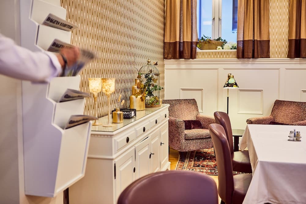 A cozy hotel lounge features elegant leopard-print armchairs, a patterned rug, and a white cabinet adorned with golden lamps, creating a warm and inviting atmosphere ideal for travelers seeking relaxation.