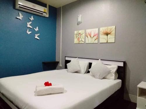 A cozy hotel room features a neatly made bed adorned with a red flower, set against a calming blue wall decorated with white butterflies and floral artwork, ideal for travelers seeking comfort and relaxation.