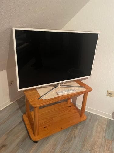 A cozy indoor corner features a modern flat-screen TV on a wooden stand with remote controls, ideal for travelers seeking relaxation in a comfortable apartment setting.