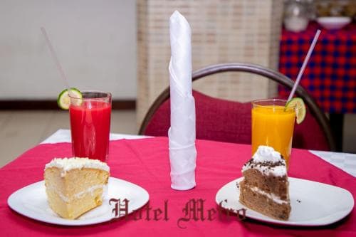 A cozy café scene features two slices of cake paired with vibrant fruit juices on a red tablecloth, evoking a relaxed dining atmosphere ideal for travelers seeking a sweet treat during their journey.