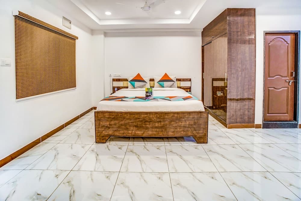 A cozy hotel bedroom features a neatly made bed with colorful pillows, marble flooring, wooden furnishings, and a serene ambiance ideal for travelers seeking comfort and relaxation.