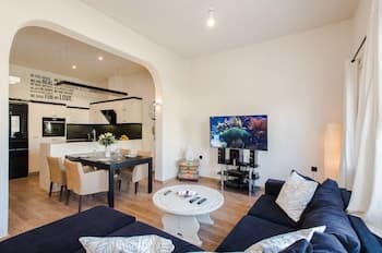 A cozy modern apartment features an open-plan living space with a comfortable sofa, dining area, and kitchen, creating a welcoming atmosphere ideal for travelers seeking a homey stay.