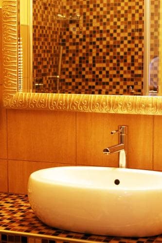A luxurious bathroom features a sleek white sink, ornate mosaic tiles, and a large mirror, creating an elegant ambiance ideal for high-end hotel stays or spa retreats.