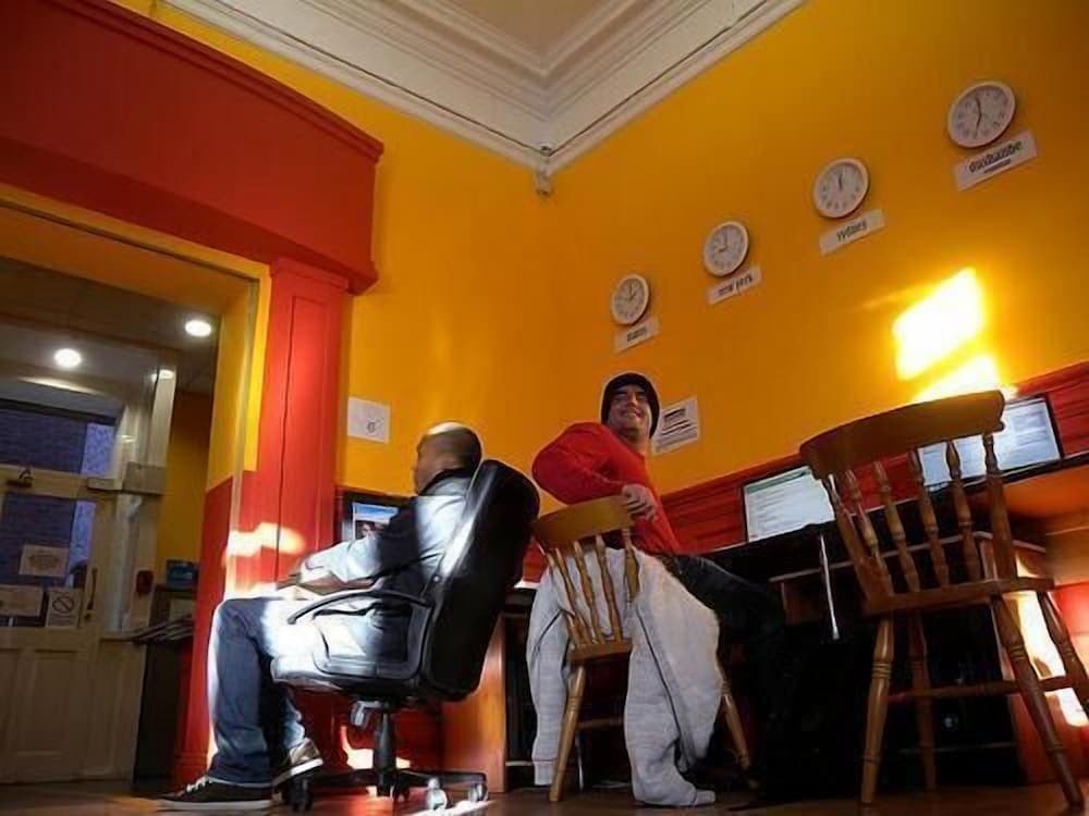 A cozy internet café with vibrant yellow walls adorned with world clocks sets a warm, inviting mood as travelers relax in chairs near computers, ideal for digital nomads seeking connectivity and comfort.