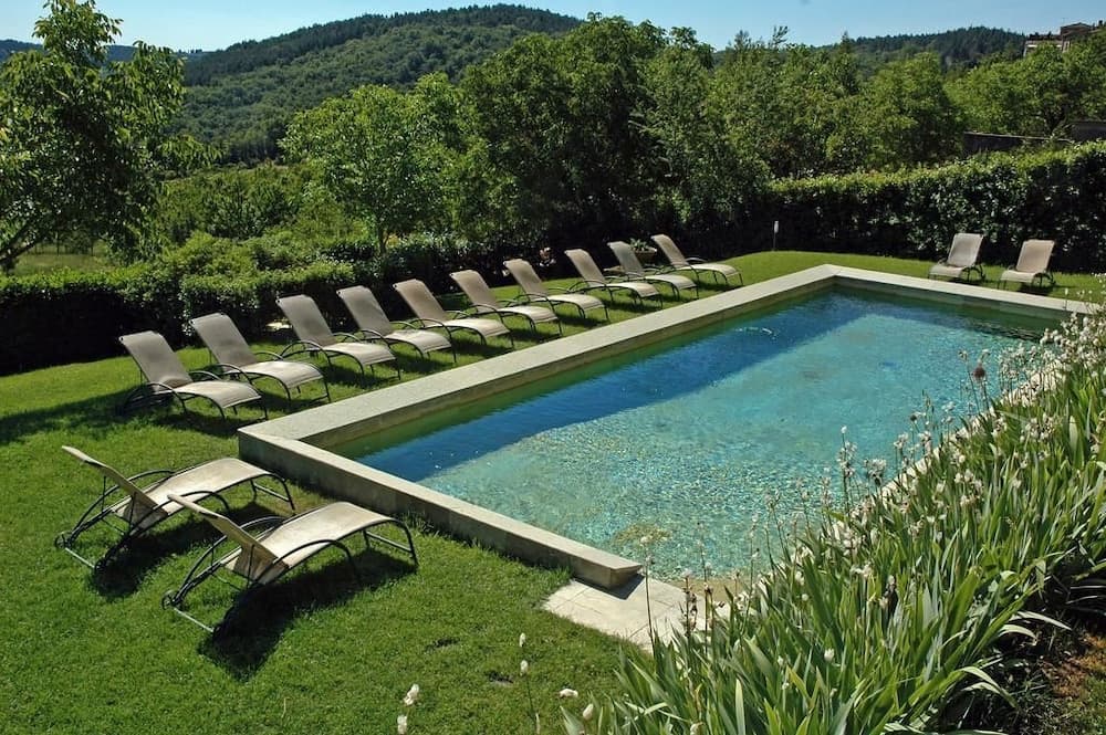 A serene outdoor pool surrounded by lush greenery and lined with lounge chairs invites relaxation in a tranquil countryside retreat, perfect for vacationers seeking peace and natural beauty.