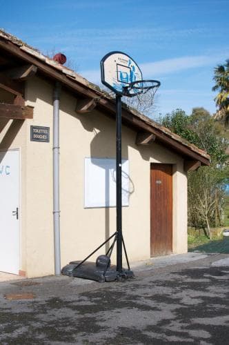 A sunny outdoor basketball hoop stands beside a rustic building with a "Toilettes Douchees" sign, offering a casual sports vibe for travelers seeking recreational activities near basic amenities.