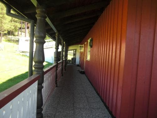 A serene rural retreat features a long, covered porch with ornate wooden pillars and red-paneled walls, ideal for travelers seeking a peaceful countryside escape.