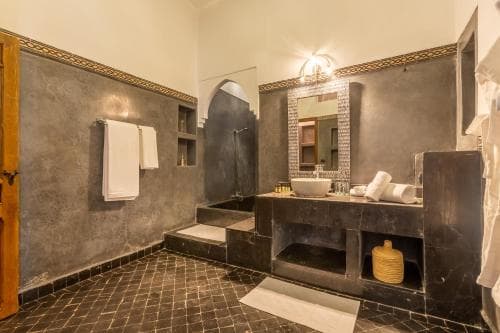 A serene, modern bathroom with dark tiled walls, an arched shower niche, and a double vanity adorned with white towels and decorative items, ideal for travelers seeking luxury accommodations.