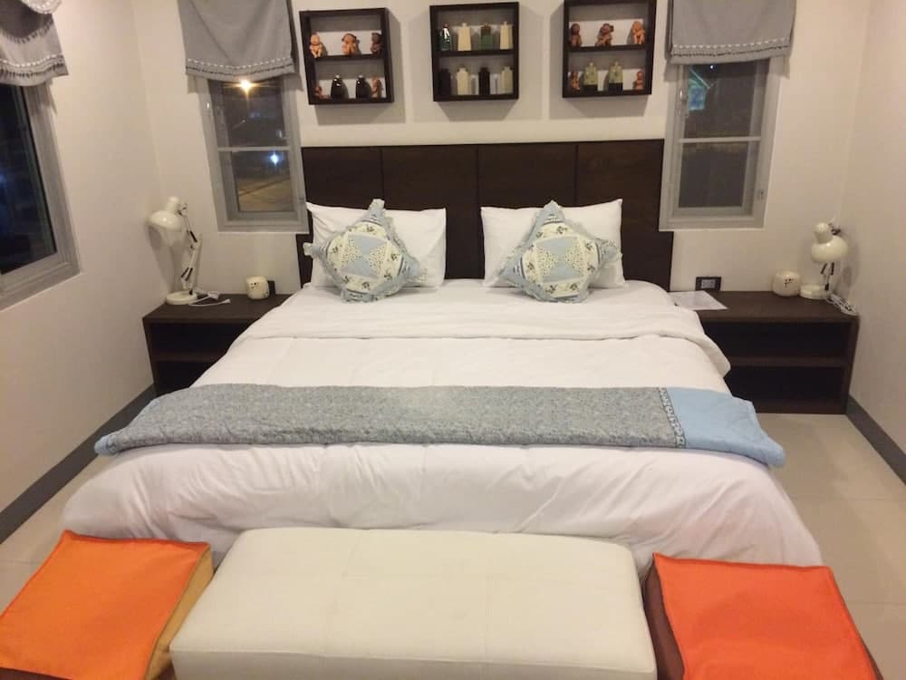 A cozy bedroom with a neatly made bed adorned with decorative pillows and a blue throw blanket, flanked by wooden nightstands with lamps and shelves displaying small figurines, ideal for travelers seeking a comfortable and stylish accommodation.