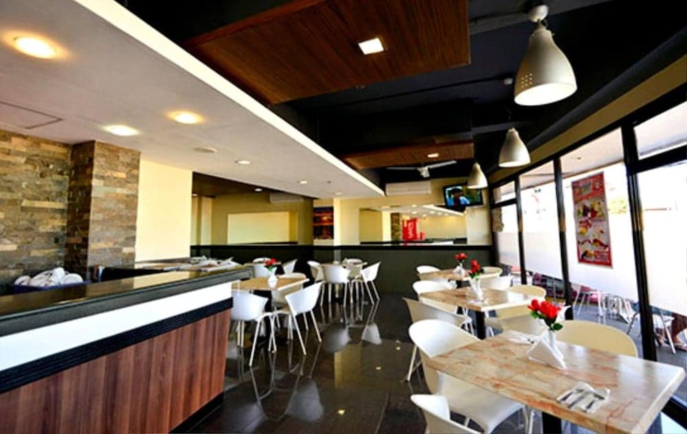A cozy indoor restaurant with modern decor, featuring white chairs, marble tables adorned with red flowers, and a sleek bar area, creates an inviting atmosphere perfect for travelers seeking a comfortable dining experience.