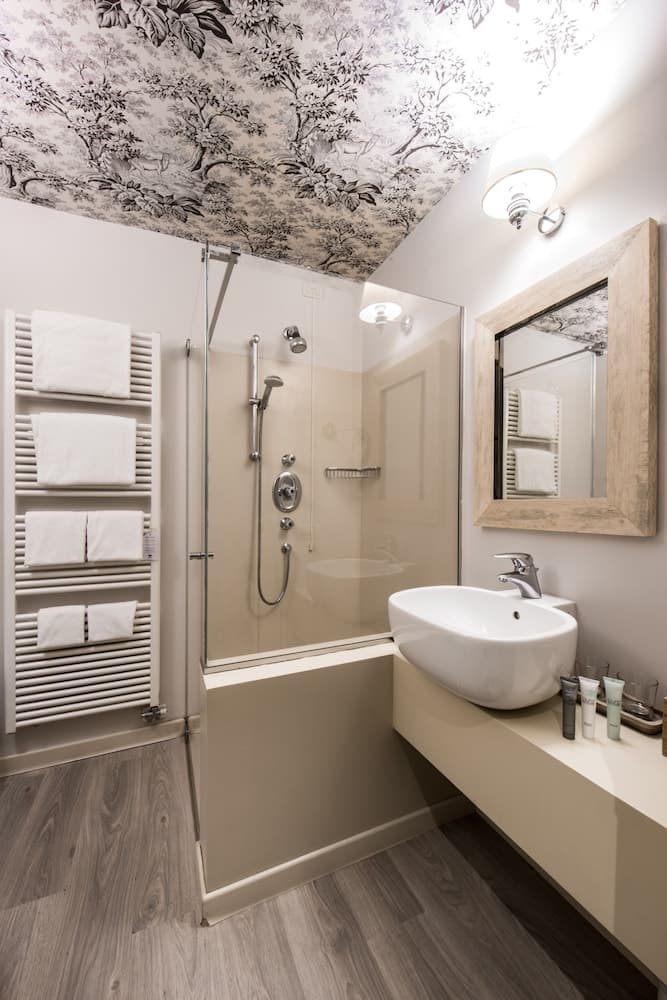 A cozy bathroom features a serene atmosphere with a glass-enclosed shower, a sleek sink, neatly folded towels on a heated rack, and a whimsical tree-patterned ceiling, ideal for travelers seeking comfort and style in their accommodations.