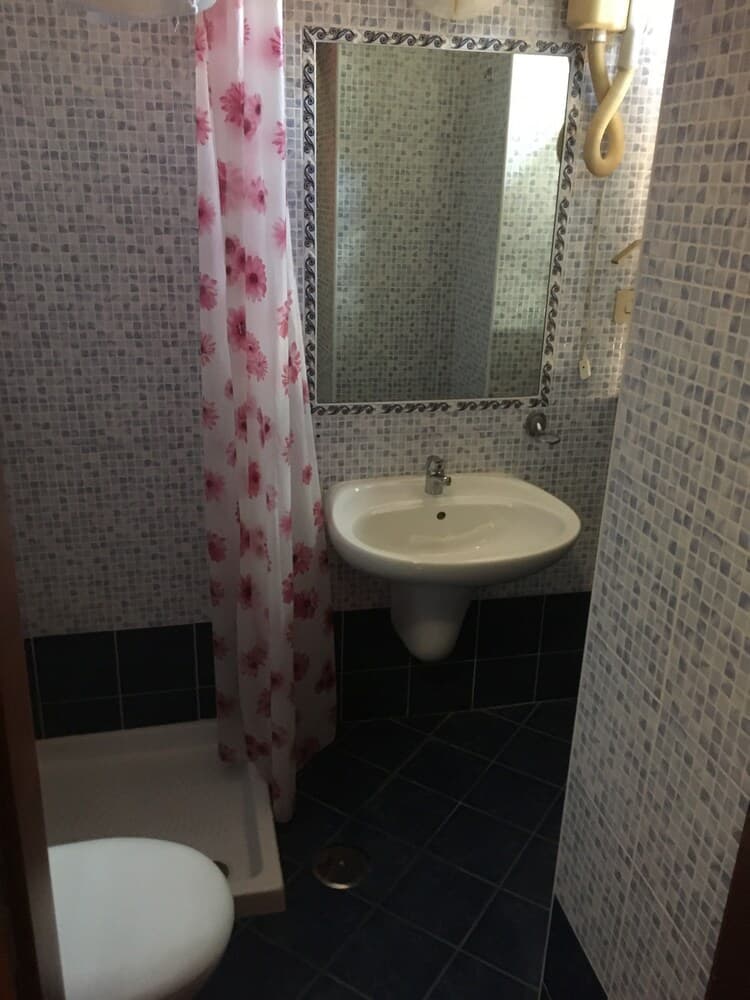 A cozy bathroom with mosaic tiles, a floral shower curtain, and a pedestal sink creates a quaint atmosphere ideal for travelers seeking a charming accommodation experience.