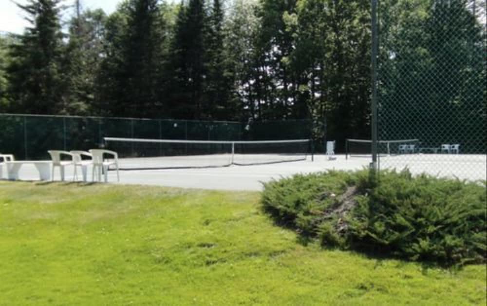 A serene outdoor tennis court surrounded by lush greenery offers a tranquil setting for sports enthusiasts, featuring white chairs and a well-maintained lawn ideal for leisurely breaks during a getaway.