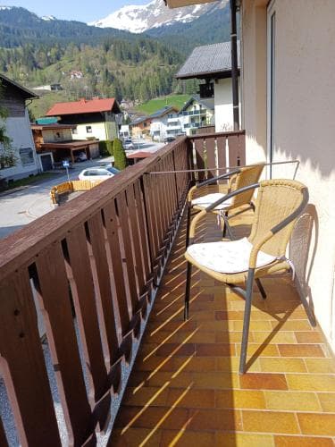 A cozy balcony with wicker chairs overlooks a quaint village nestled in a mountainous valley, ideal for travelers seeking a serene retreat with scenic views.