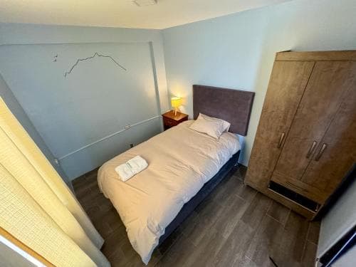 A cozy single bed in a minimalist bedroom with soft lighting, wooden flooring, and a wardrobe, ideal for travelers seeking a simple and comfortable stay.