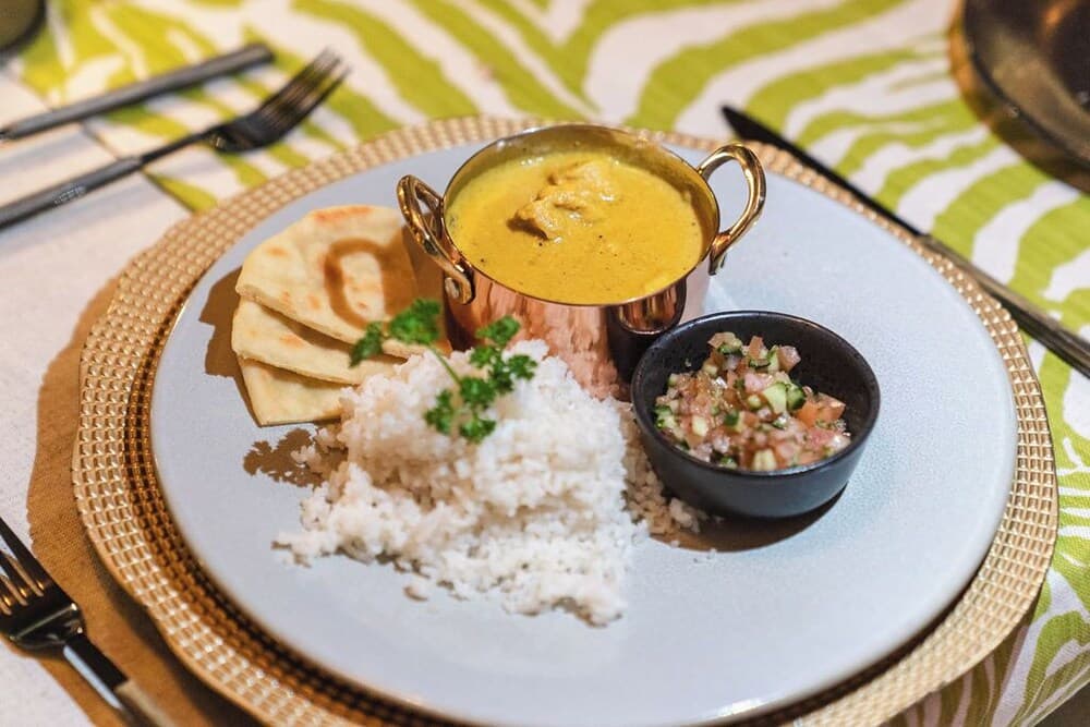 A beautifully plated dish featuring curry in a copper pot, rice, naan bread, and a fresh salsa garnish on a stylish table setting, perfect for culinary enthusiasts exploring international cuisine.