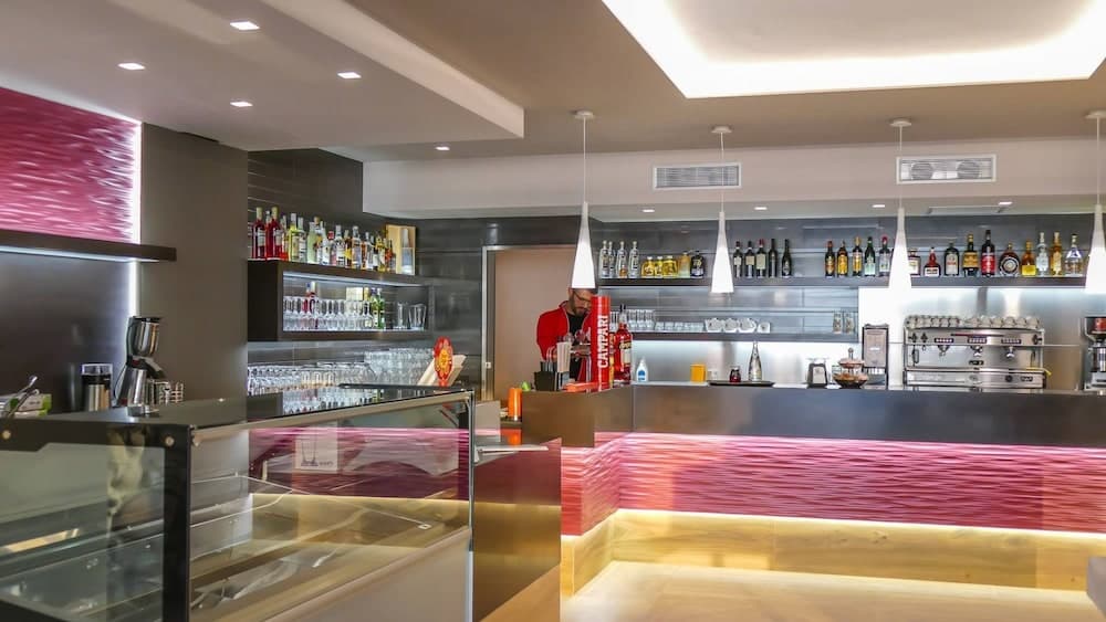A modern bar with sleek design, vibrant red accents, and well-stocked shelves creates an inviting atmosphere ideal for travelers seeking a stylish spot to unwind and enjoy drinks.