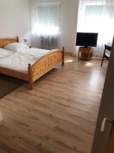 A cozy bedroom with a wooden bed, laminate flooring, and a TV near curtained windows offers a comfortable stay for travelers seeking simplicity and relaxation.
