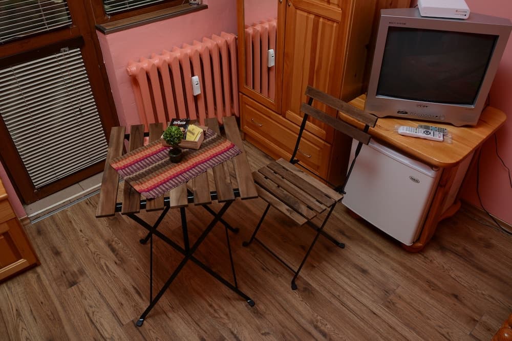 A cozy, rustic room features a wooden table set with a colorful placemat, a small TV atop a mini fridge, and warm-toned furnishings, ideal for travelers seeking a quaint and comfortable stay.