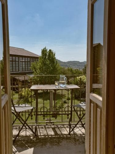 A serene balcony view opens to a lush garden with a wooden table set for relaxation, ideal for travelers seeking a peaceful countryside retreat.