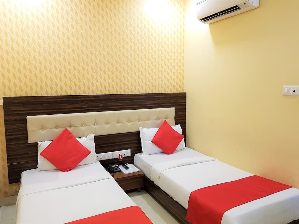 A cozy hotel room features two neatly arranged beds with red accents against a warm yellow wall, ideal for travelers seeking comfort and simplicity.