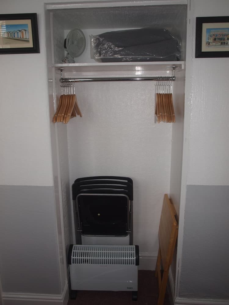 A cozy closet space with wooden hangers, a fan, stacked chairs, and a heater, ideal for travelers seeking organized storage in a compact living area.