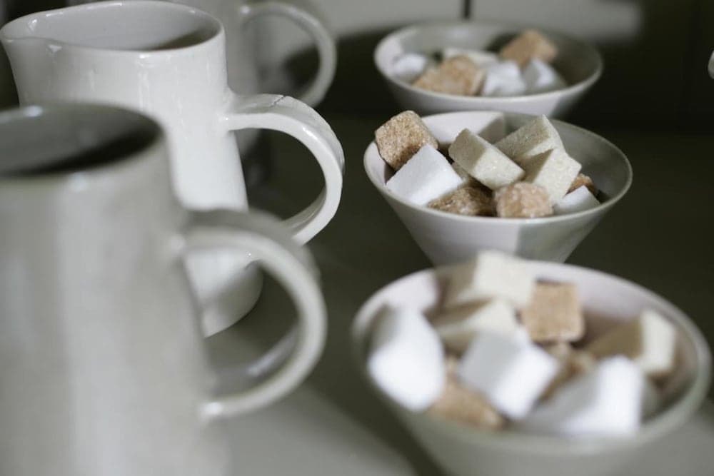 A cozy café setting features white mugs paired with bowls of sugar cubes and marshmallows, creating an inviting atmosphere perfect for travelers seeking a warm beverage experience.