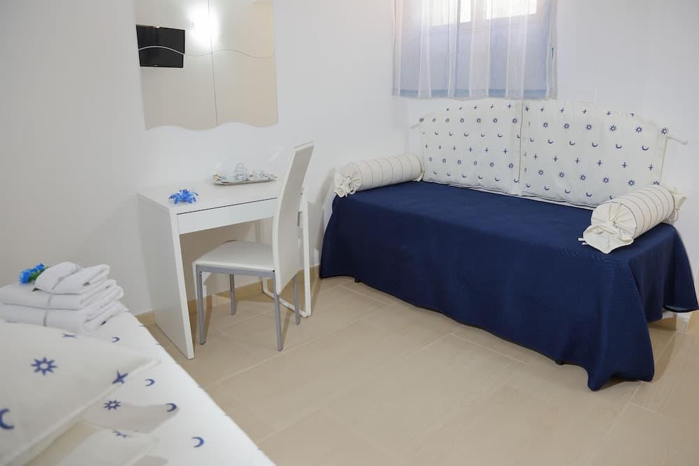 A cozy hotel room features a navy blue bedspread, white furniture, and soft natural light filtering through sheer curtains, creating a serene and inviting atmosphere ideal for relaxation.