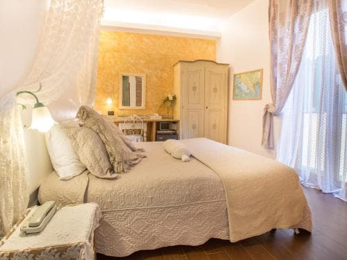 A cozy bedroom with warm yellow walls, elegant lace curtains, and a neatly made bed creates an inviting atmosphere, perfect for travelers seeking a comfortable and charming accommodation experience.