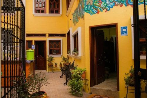 A vibrant yellow courtyard adorned with colorful murals, potted plants, and ornate windows exudes a cozy, artistic charm ideal for travelers seeking a unique boutique accommodation experience.