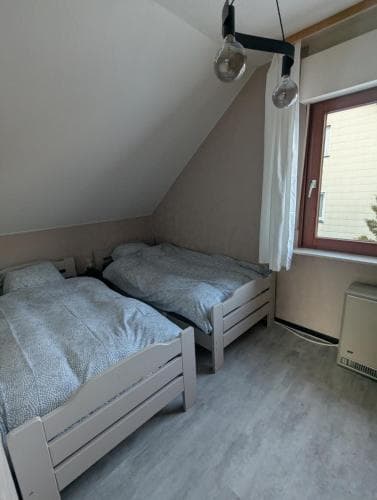 A cozy attic bedroom with two single beds under slanted ceilings, simple pendant lights, and a window offering natural light, ideal for budget-friendly travelers seeking a quaint and comfortable stay.