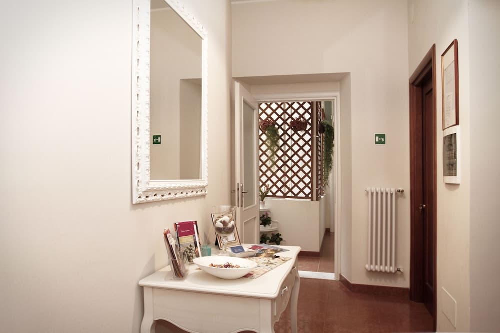 A cozy hotel hallway features a white console table adorned with decorative items, a large ornate mirror, and a lattice window with greenery, creating an inviting and serene atmosphere ideal for travelers seeking comfort.