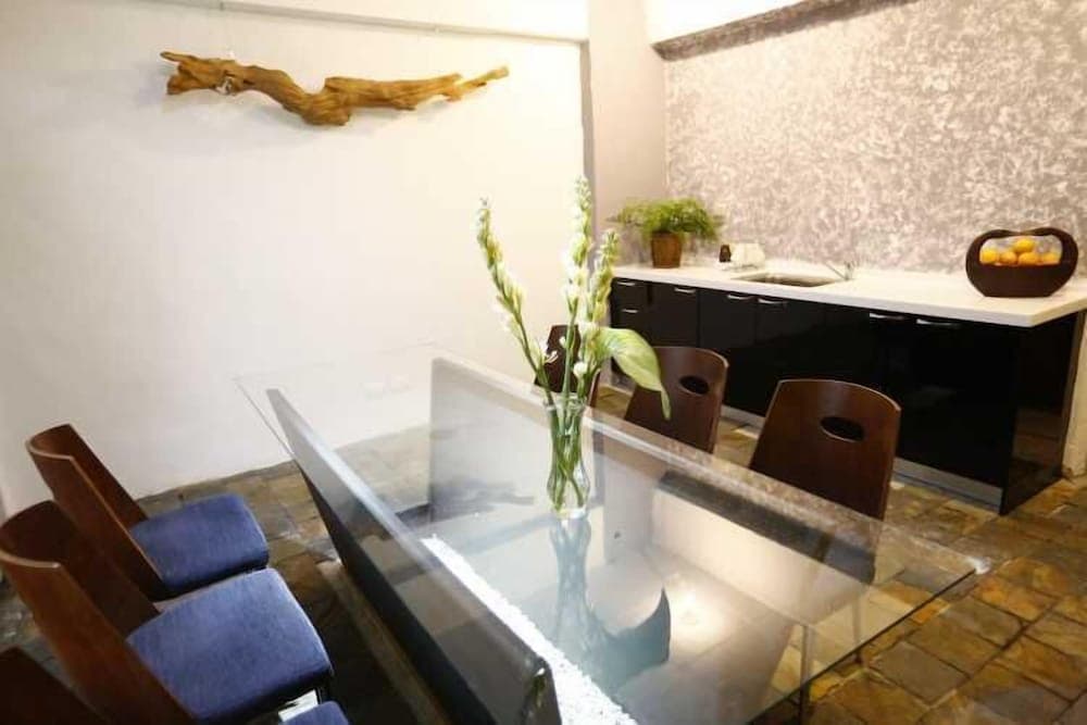 A cozy dining area with a sleek glass table, wooden chairs, and a modern kitchenette exudes a serene ambiance, perfect for travelers seeking a tranquil retreat with stylish decor and natural accents like driftwood art and fresh flowers.