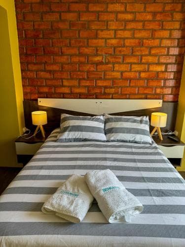 A cozy bedroom with a brick accent wall, striped bedding, and warm lighting creates an inviting atmosphere, ideal for travelers seeking comfort in boutique accommodations.