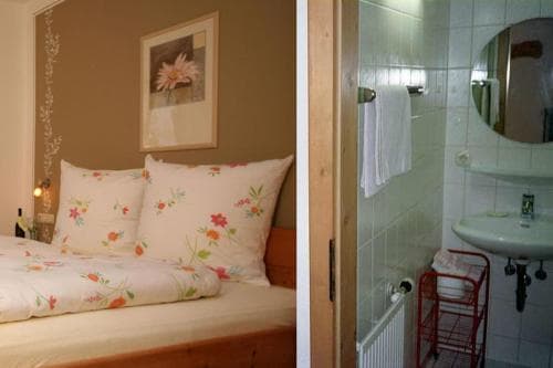 A cozy bedroom with floral bedding and warm lighting adjoins a compact bathroom with tiled walls, ideal for travelers seeking comfort in a quaint accommodation setting.