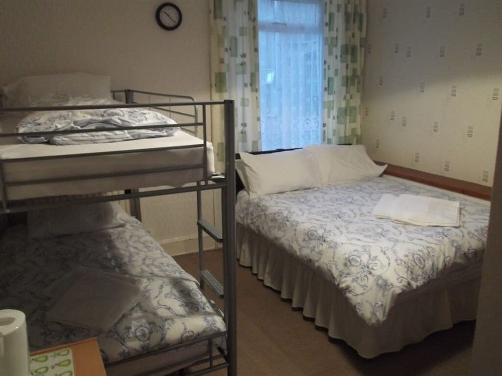 A cozy hostel room features a bunk bed and a double bed with patterned bedding, soft lighting from sheer curtains, and a tidy atmosphere ideal for budget travelers seeking comfort.