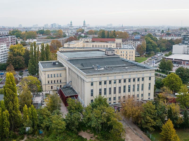 Aerial view of an urban landscape featuring a large, historic building surrounded by lush greenery, ideal for travelers exploring Berlin's architectural and cultural landmarks.